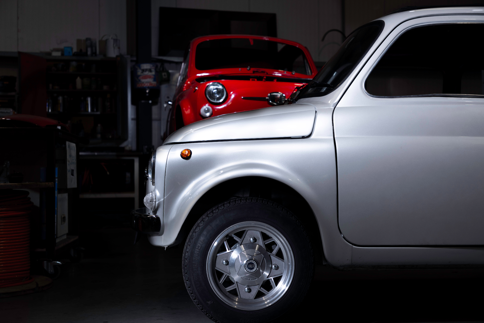 Silver classic Fiat 500 in the Silent Classics workshop with a red 500 behind